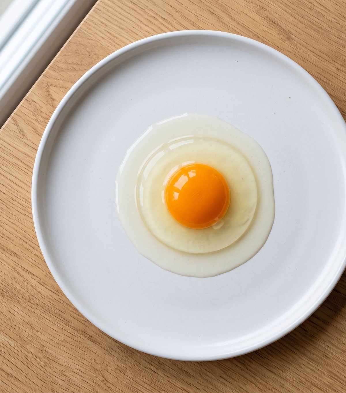 A fresh egg cracked onto a white plate: a tall, domed, deep-orange yolk